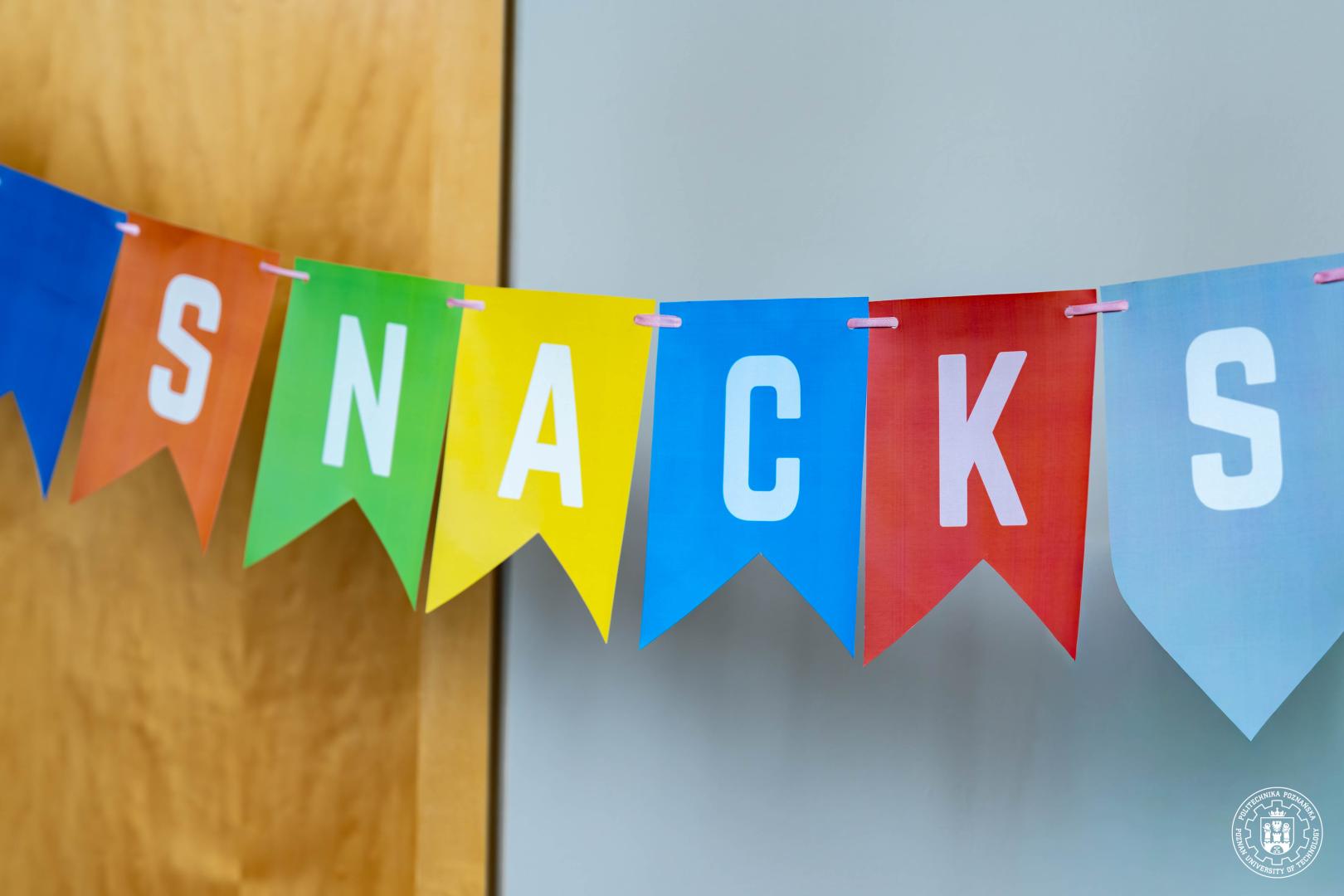 A colorful bunting banner made of flags forming the word "SNACKS", indicating the place with refreshments for the participants.