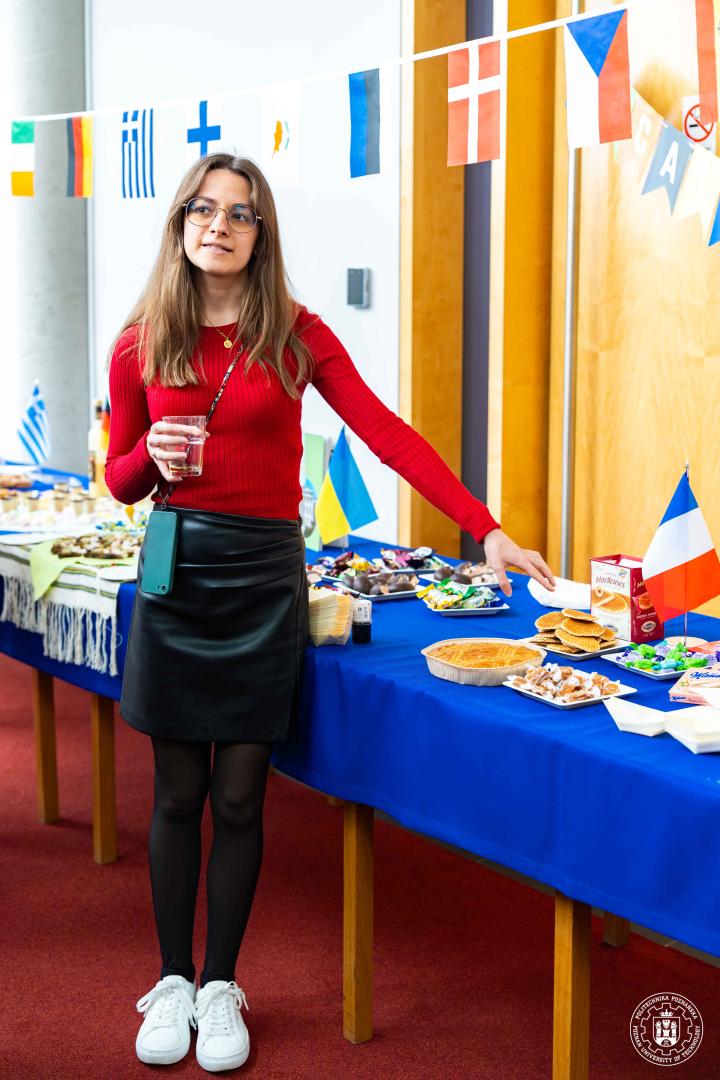 A female participant in a red blouse presenting a table with French sweets and snacks.