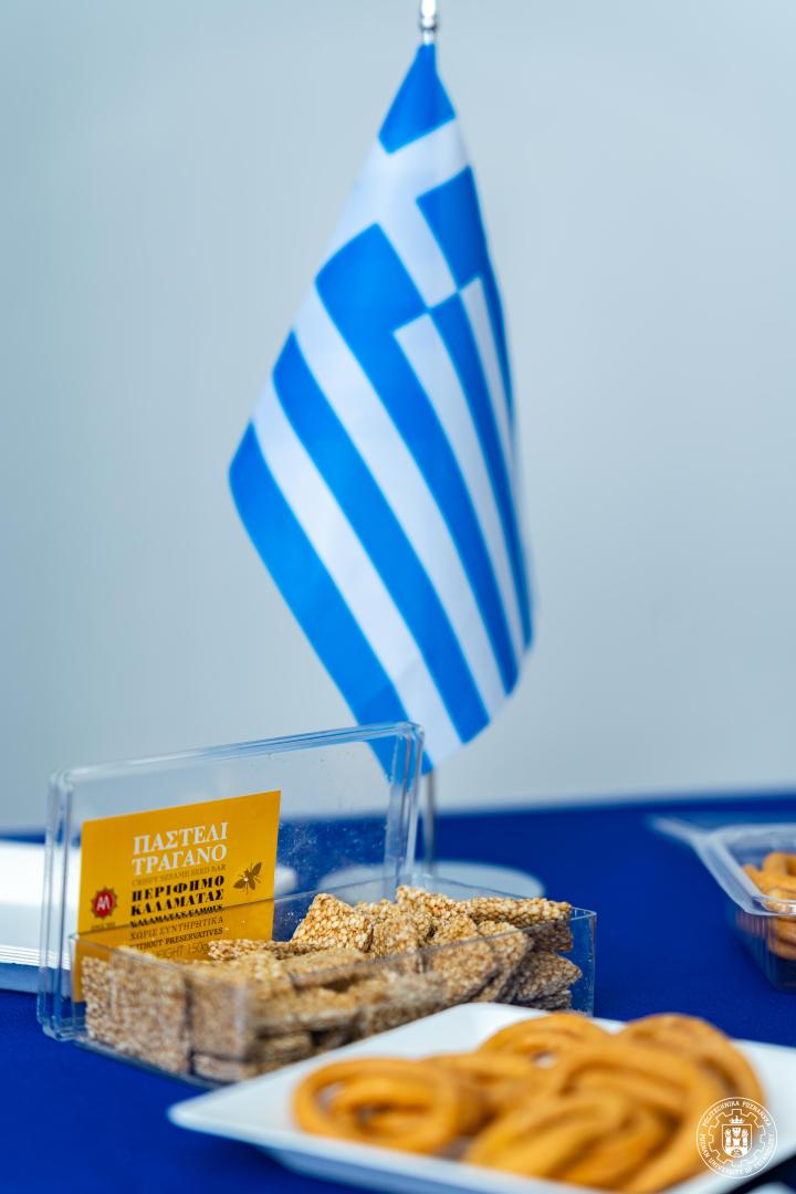 A small Greek flag standing on a table next to traditional snacks during a refreshment session.
