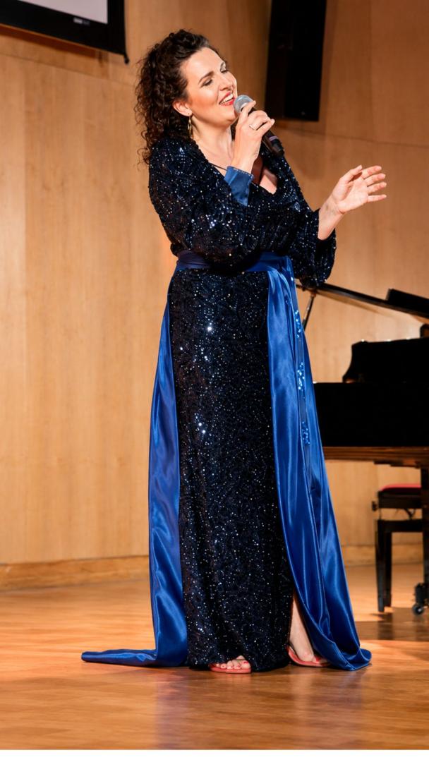 Marta Florek śpiewa na scenie do mikrofonu w granatowej, błyszczącej sukni z długim trenem.