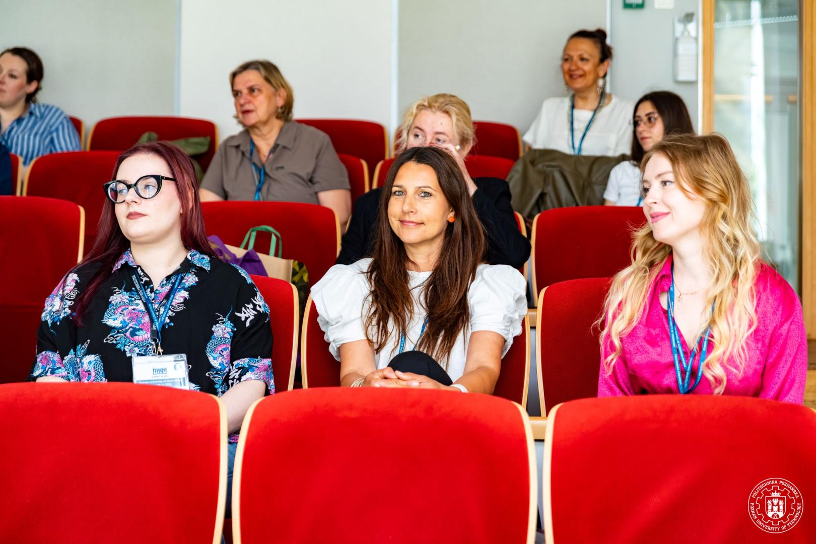 Female participants sitting in the seats of a lecture hall and listening to a presentation during a meeting.