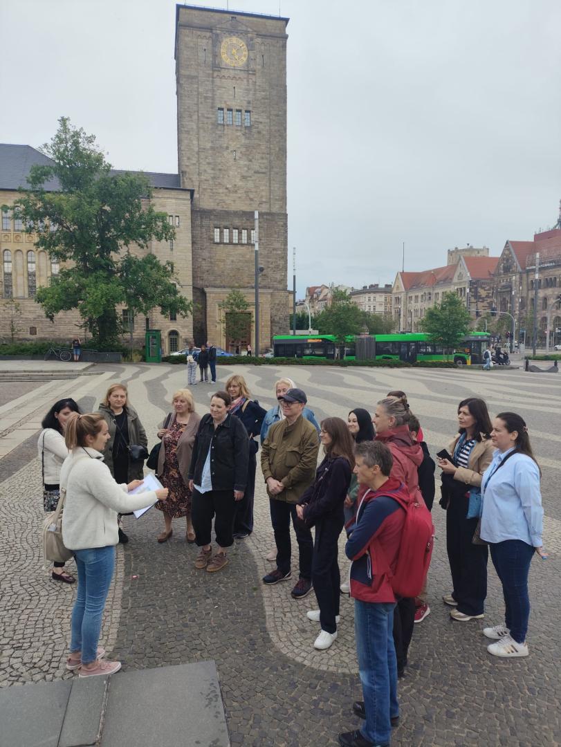 A group of participants listening to a tour guide during a sightseeing tour of Poznań in the square in front of the Imperial Castle.