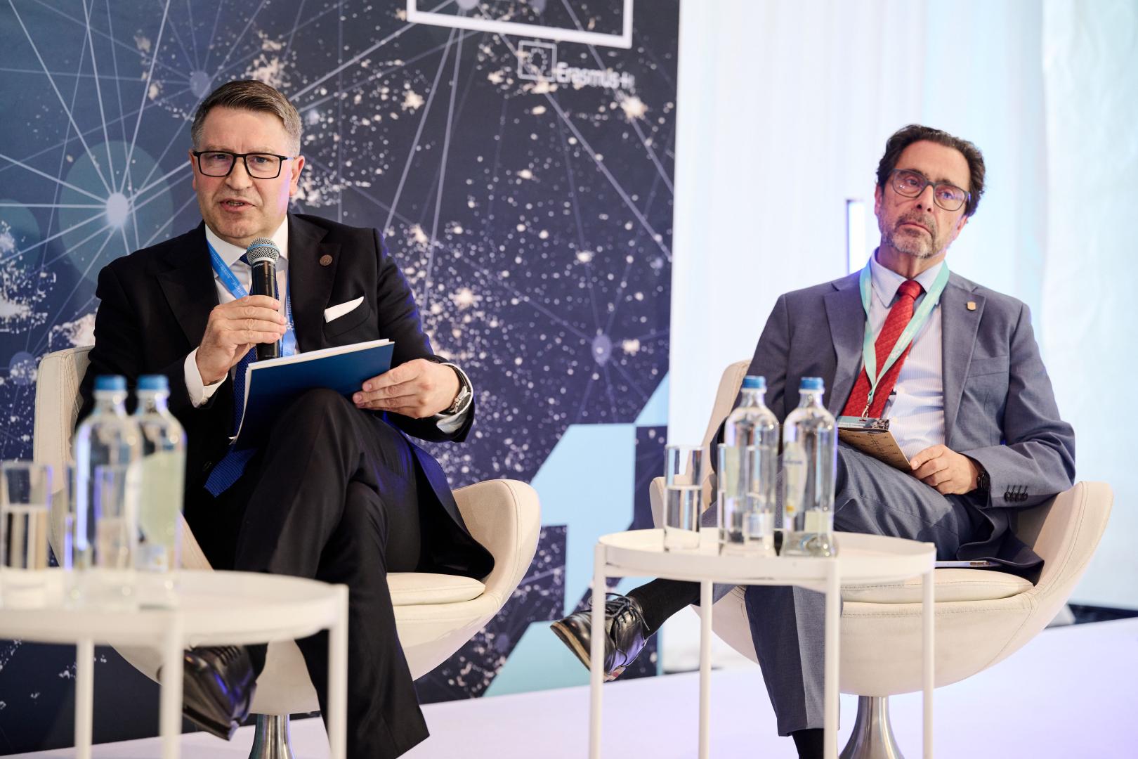 Debata panelowa w Brukseli z udziałem Rektora Politechniki Poznańskiej (z mikrofonem) na tle ściany z logotypem Erasmus+.