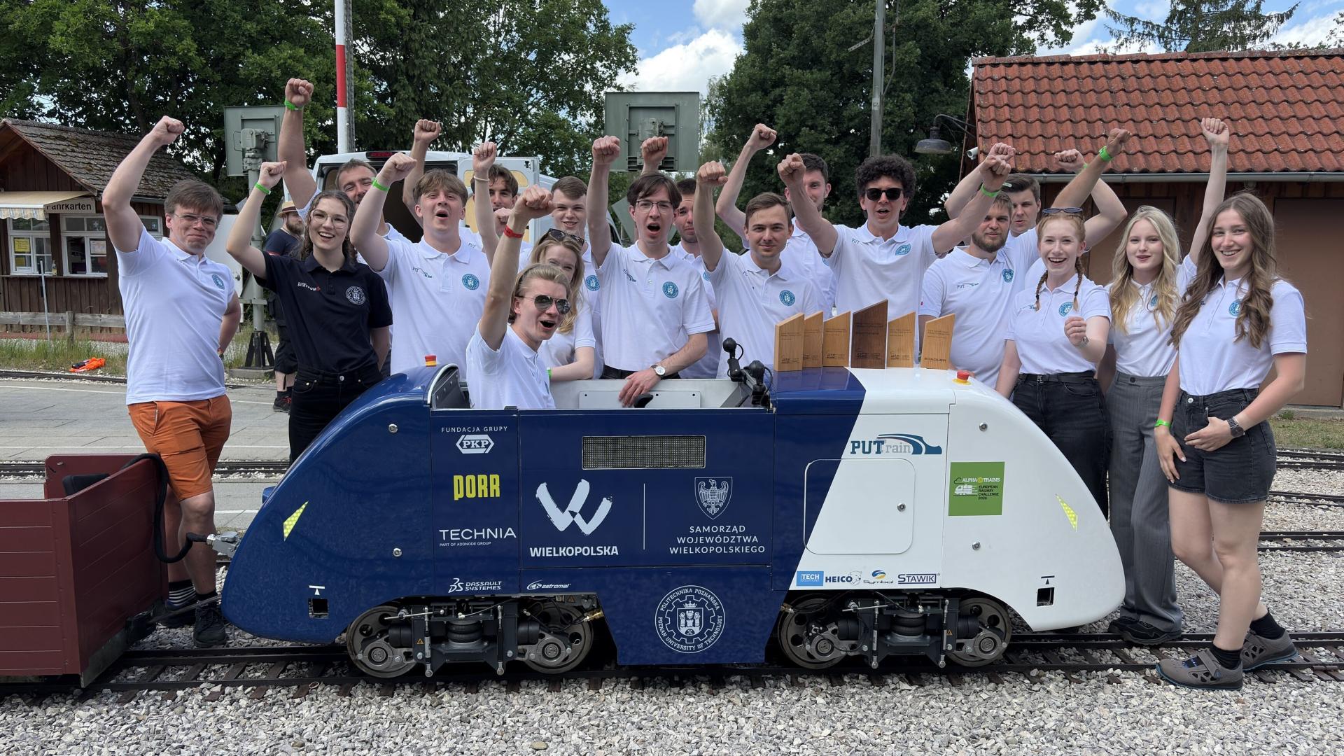 Studenci z zespołu PUTrain pozujący z miniaturową lokomotywą i zdobytymi pucharami.