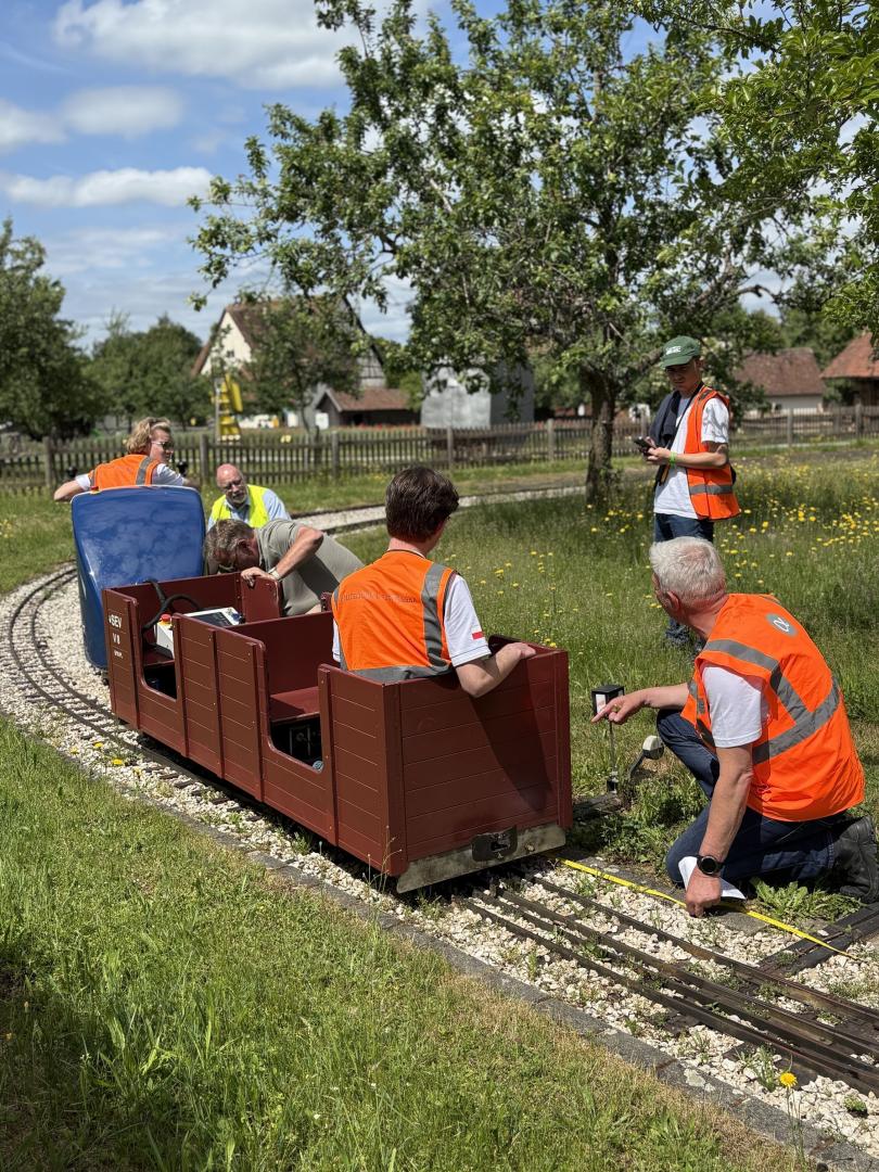 Sędziowie i uczestnicy sprawdzający miniaturowy wagon na torze podczas zawodów.