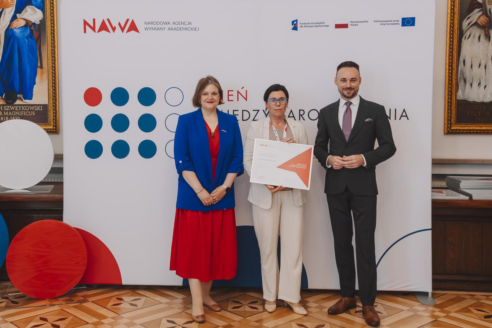 Wręczenie certyfikatu podczas wydarzenia NAWA „Dzień Umiędzynarodowienia” na tle oficjalnej ścianki konferencyjnej.