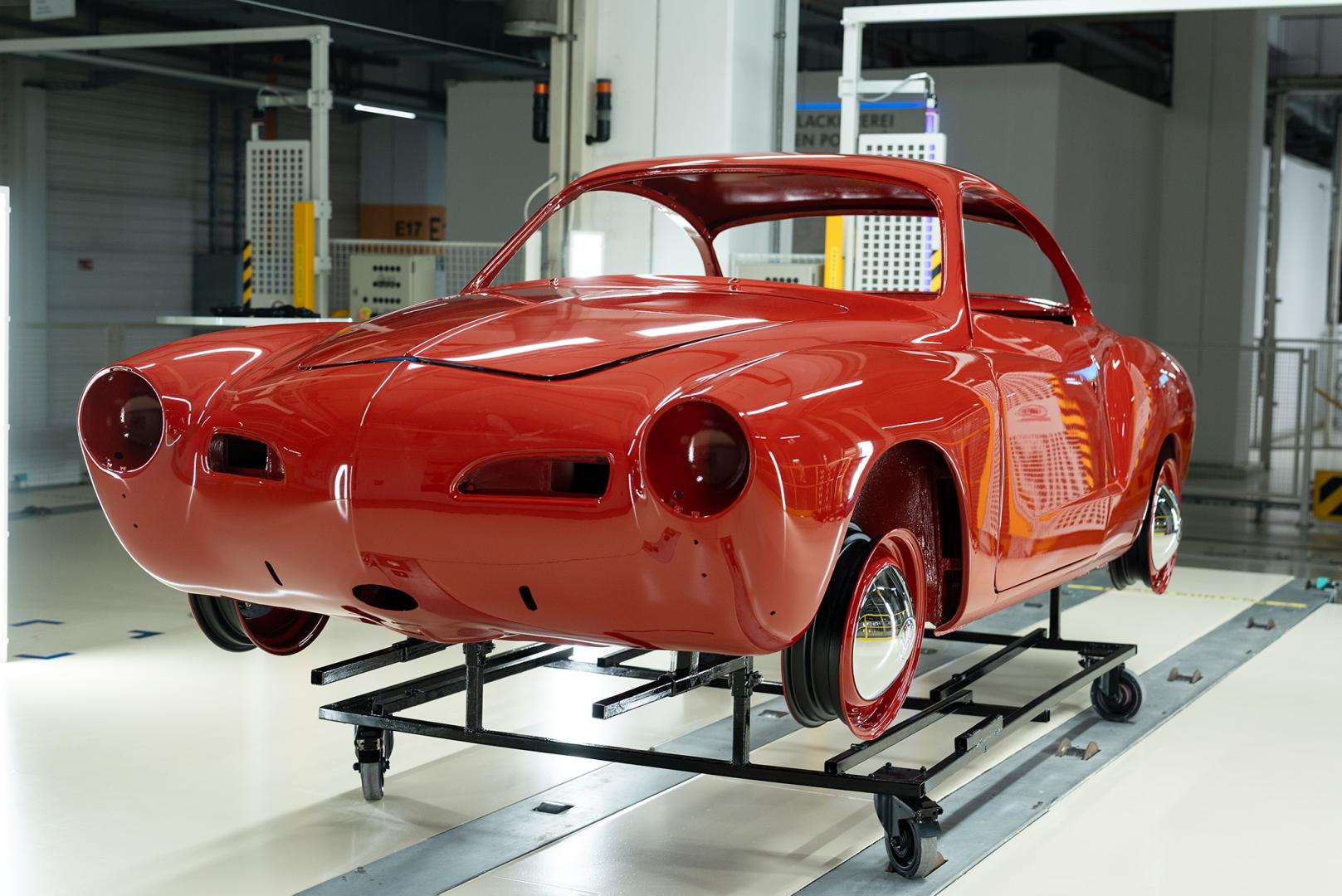 Odrestaurowana, czerwona karoseria zabytkowego Volkswagena Karmann Ghia wyeksponowana na wózku technologicznym wewnątrz jasnej hali lakierni.