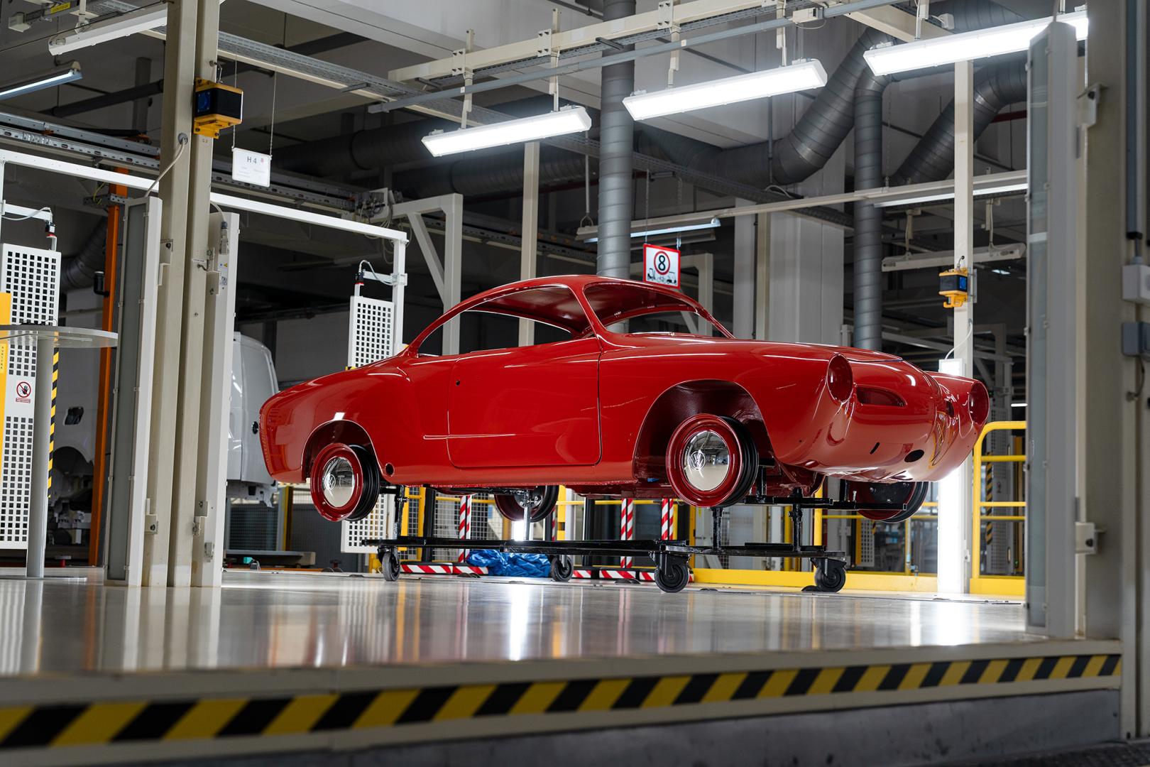 Odrestaurowana, czerwona karoseria zabytkowego Volkswagena Karmann Ghia wyeksponowana na wózku technologicznym wewnątrz jasnej hali lakierni.