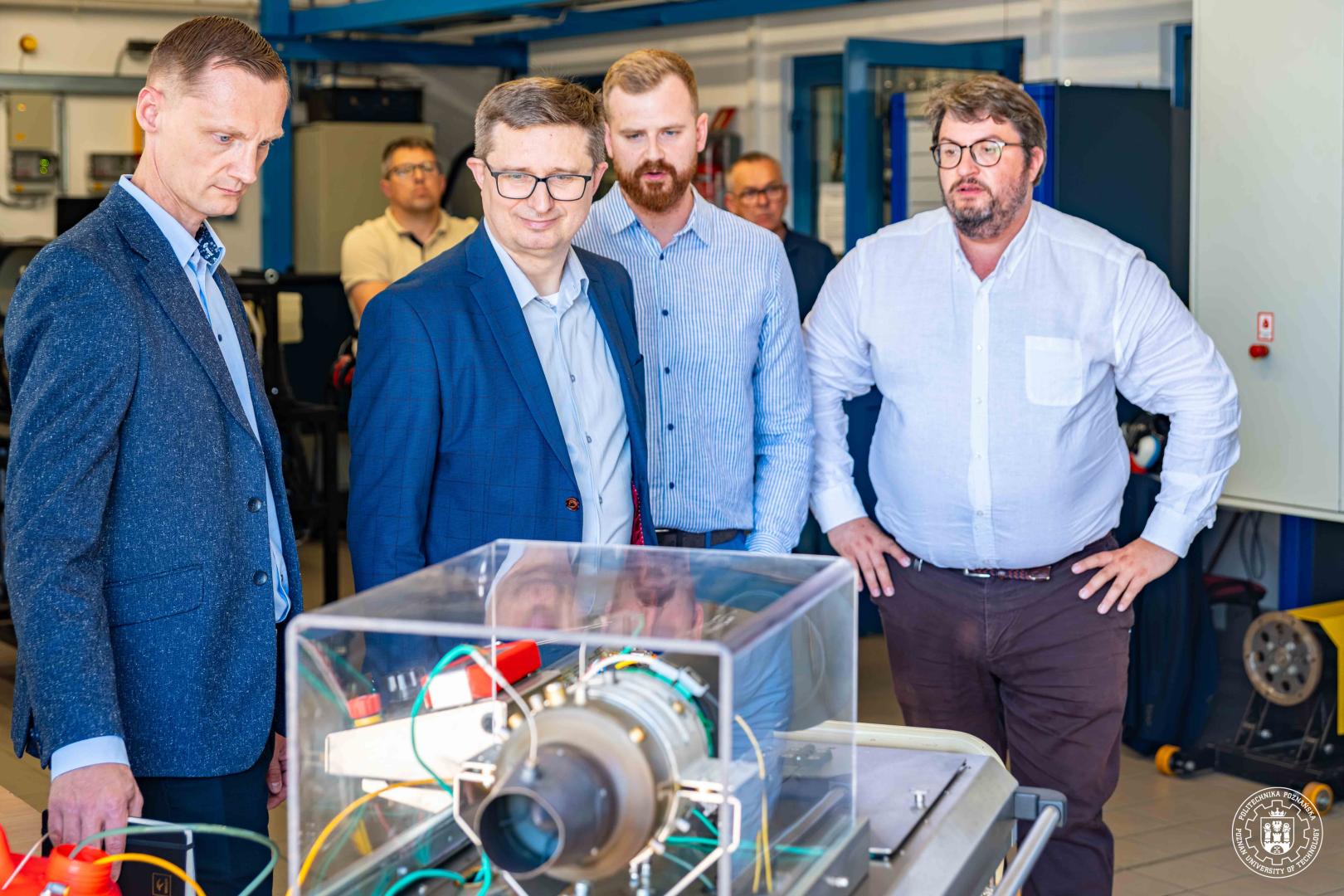 Rektor Teofil Jesionowski i przedstawiciele ORLEN S.A. oglądają mini silnik odrzutowy w laboratorium Politechniki Poznańskiej.