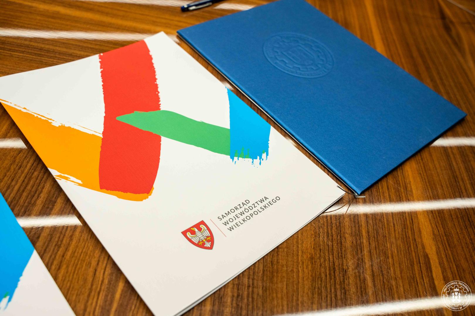Dokumenty z logo Samorządu Województwa Wielkopolskiego i Politechniki Poznańskiej na stole.