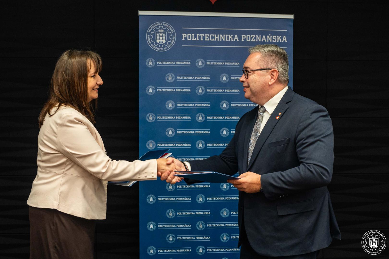 Sygnatariusze podają sobie dłonie na tle logo Politechniki Poznańskiej