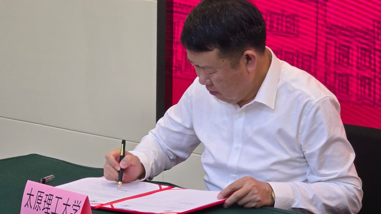 Prof. Shen podpisuje dokument na stole, obok widoczna tabliczka z napisem "Taiyuan University of Technology".