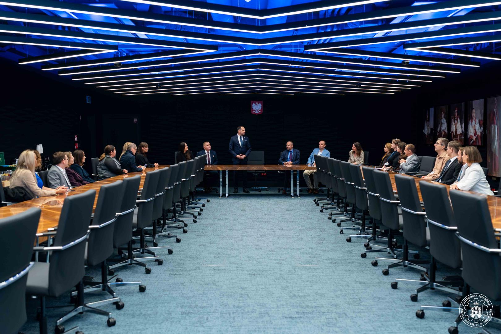 Uczestnicy spotkania inauguracyjnego projektu przy długim stole konferencyjnym podczas przemówienia otwierającego na Politechnice Poznańskiej.