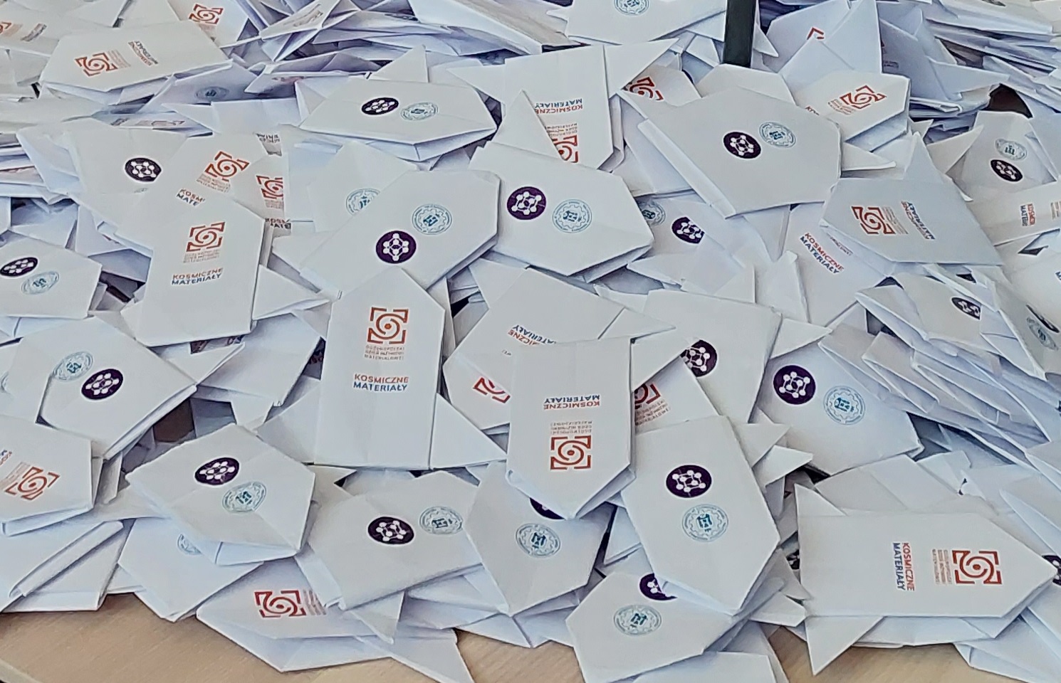 Stos papierowych rakiet origami z logotypami i napisem „Kosmiczne Materiały”, przygotowanych w ramach wydarzenia.