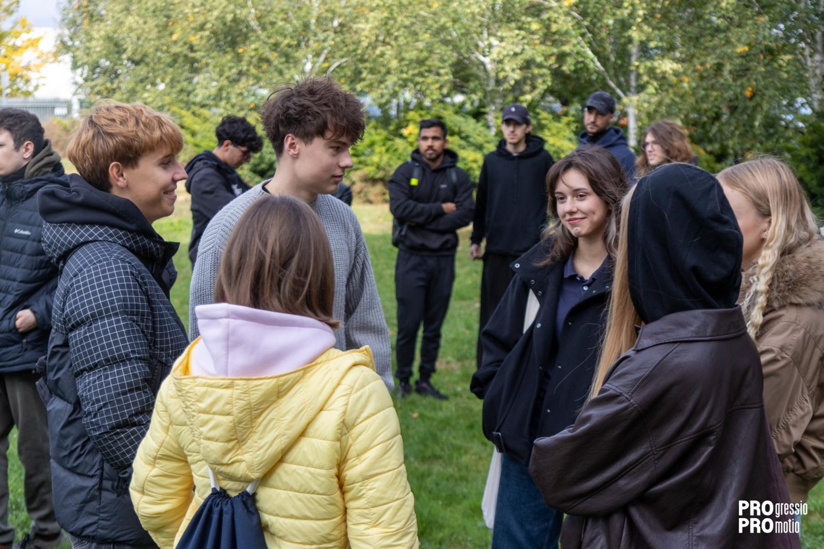 A group of young students talks and integrates in a circle on a green area during a campus game.