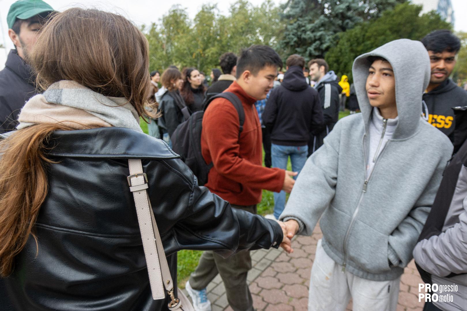 Two international students shake hands in greeting during an outdoor integration event.