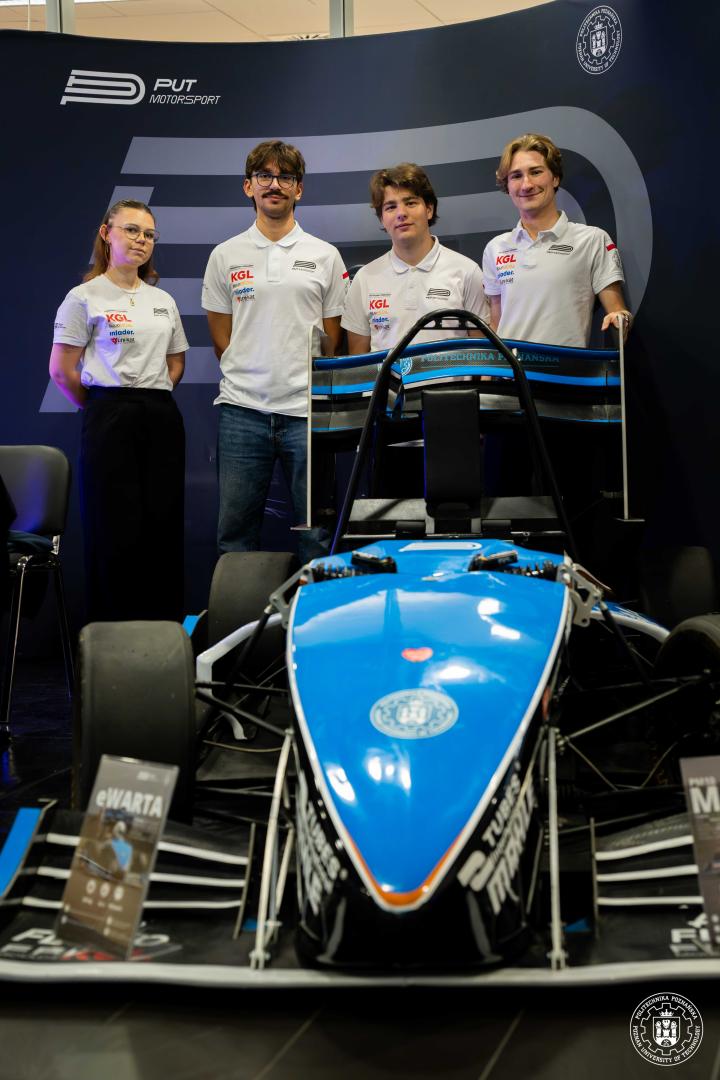 Czterech studentów stoi za niebieskim bolidem wyścigowym z napisem "PUT MOTORSPORT" i "eWARTA", wszyscy ubrani w koszulki polo z logo zespołu.