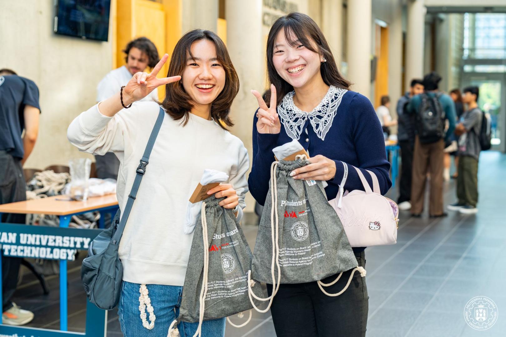 Dwie uśmiechnięte studentki zagraniczne pozują z upominkami powitalnymi podczas Orientation Day.
