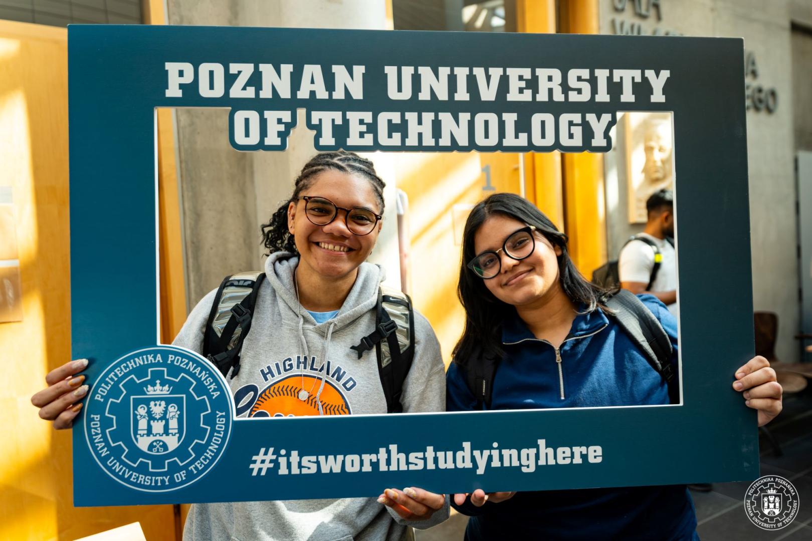 Dwie uśmiechnięte zagraniczne studentki trzymają ramkę z napisem Poznan University of Technology