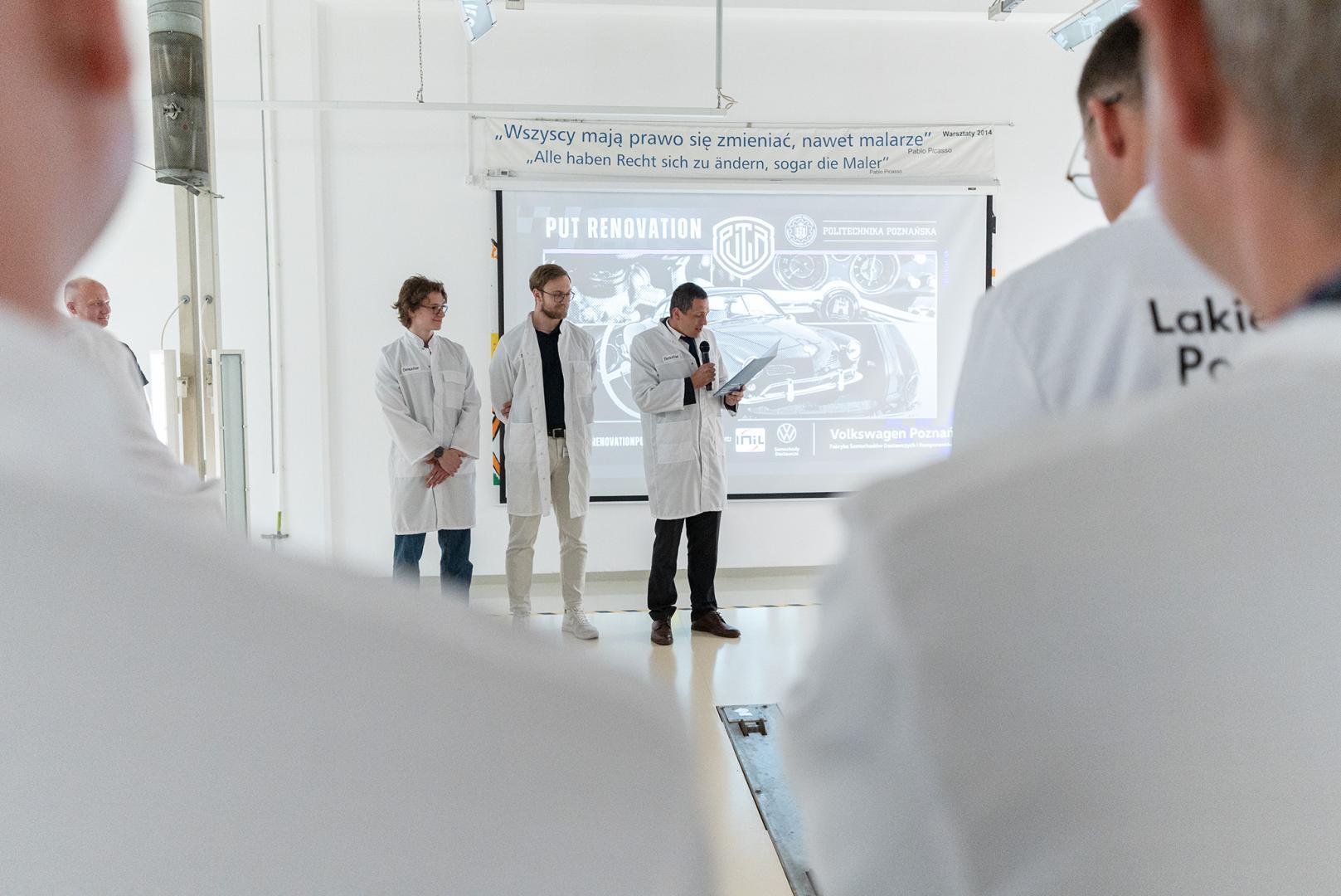 Studenci koła PUT Renovation w białych fartuchach prezentują projekt renowacji, przemawiając do mikrofonu na tle ekranu z napisem PUT RENOVATION.