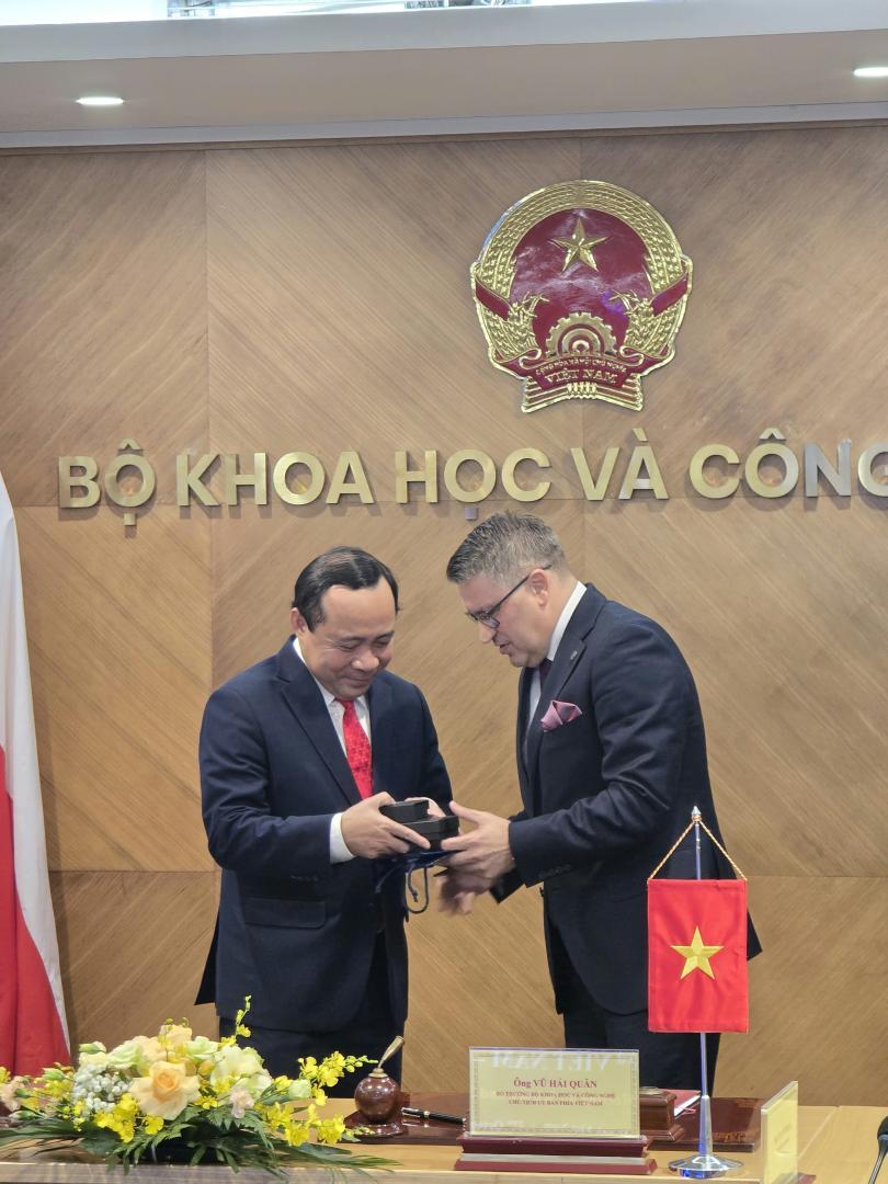 Rektor Politechniki Poznańskiej wręcza pamiątkowy upominek Ministrowi Nauki i Technologii Wietnamu na tle godła i napisu Ministerstwa w Hanoi.