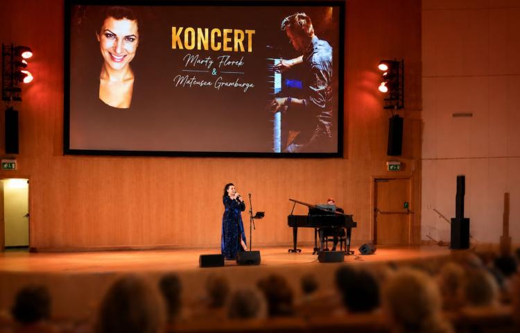Koncert Marty Florek i Mateusza Gramburga na scenie z fortepianem; publiczność ogląda występ z widowni.
