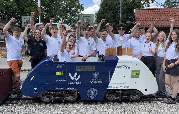 Studenci z zespołu PUTrain pozujący z miniaturową lokomotywą i zdobytymi pucharami.