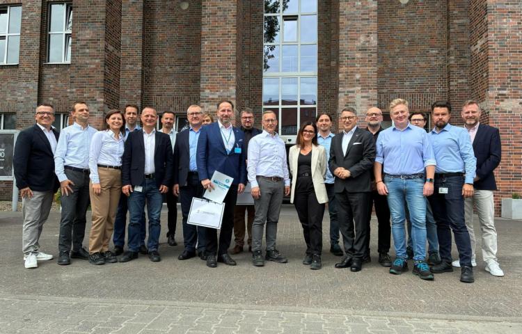 Uczestnicy spotkania z Politechniki Poznańskiej oraz Odlewni Volkswagen Poznań stoją przed ceglanym budynkiem do wspólnego zdjęcia grupowego.