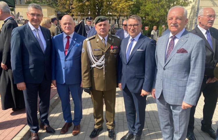 Grupa sześciu mężczyzn w oficjalnych strojach stoi na zewnątrz przed budynkami, wśród nich prof. Teofil Jesionowski (czwarty od lewej) w ciemnoniebieskim garniturze. Obok niego mężczyzna w mundurze wojskowym khaki z beretem i odznakami.