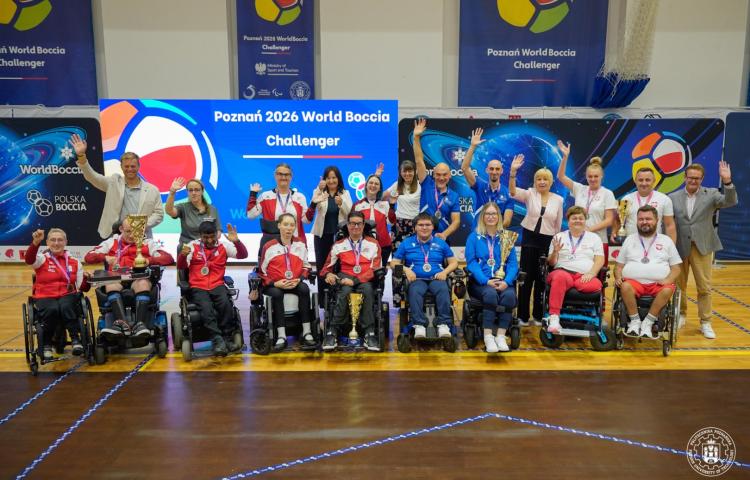 Grupa sportowców i organizatorów pozująca na parkiecie hali sportowej podczas ceremonii zakończenia Poznań 2026 World Boccia Challenger, w tym prof. Agnieszka Misztal z uniesionymi rękami, zawodnicy na wózkach inwalidzkich z medalami i pucharami oraz banery z napisem "Poznań 2026 World Boccia Challenger" i logo World Boccia, Ministerstwa Sportu i Turystyki oraz Politechniki Poznańskiej.