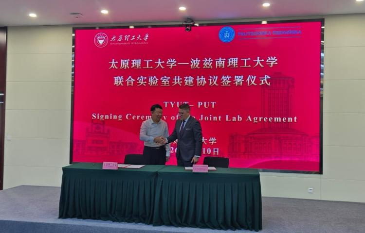 Dwóch mężczyzn – prof. Jesionowski i prof. Shen – podaje sobie dłonie przy stole z dokumentami, na tle ekranu z napisem "TYUT-PUT Signing Ceremony of Joint Lab Agreement".