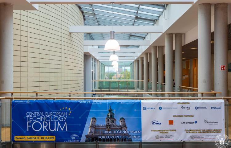 Baner konferencji CETEF’26 z podziałem na dwie części: po lewej niebieska z białym napisem nazwy konferencji, datą i logo Parlamentu Europejskiego, po prawej zdjęcie poznańskiego ratusza z hasłem "HIGH TECHNOLOGIES FOR EUROPE'S SECURITY". Baner zawieszony we wnętrzu nowoczesnego budynku z wysokim, przeszklonym sufitem i kolumnami.